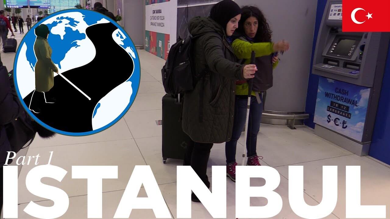 An image of Mona with her luggage and cane asking a local for help in the bus depot. In the top left corner is the PTC Logo. A cartoon Mona with her cane walking across a street on a globe. In the top right is the flag of Turkey.  